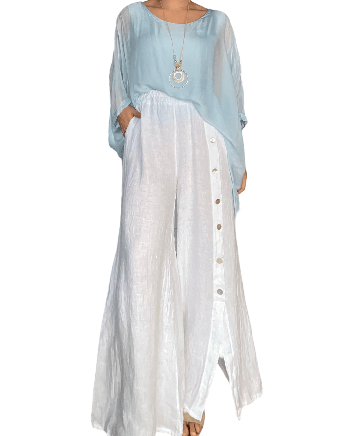 Pantalon palazzo blanc avec boutons sur le côté pour femme avec blouse et collier.