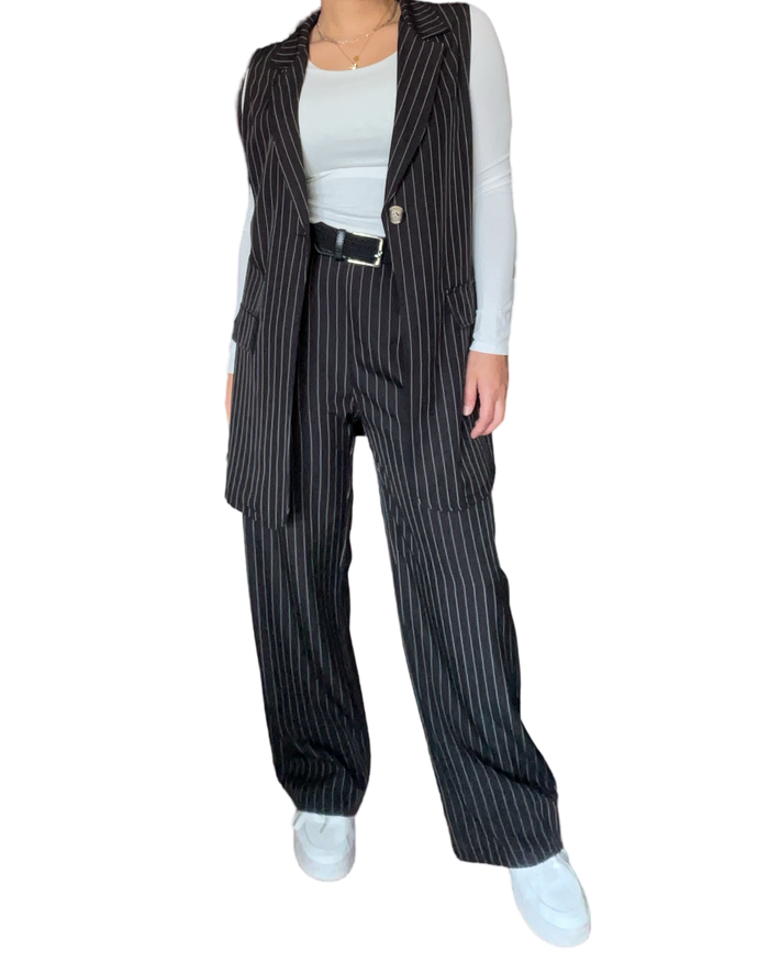 Pantalon gris à carreaux noirs pour femme à taille élastique avec chandail blanc à manche longue et ceinture.