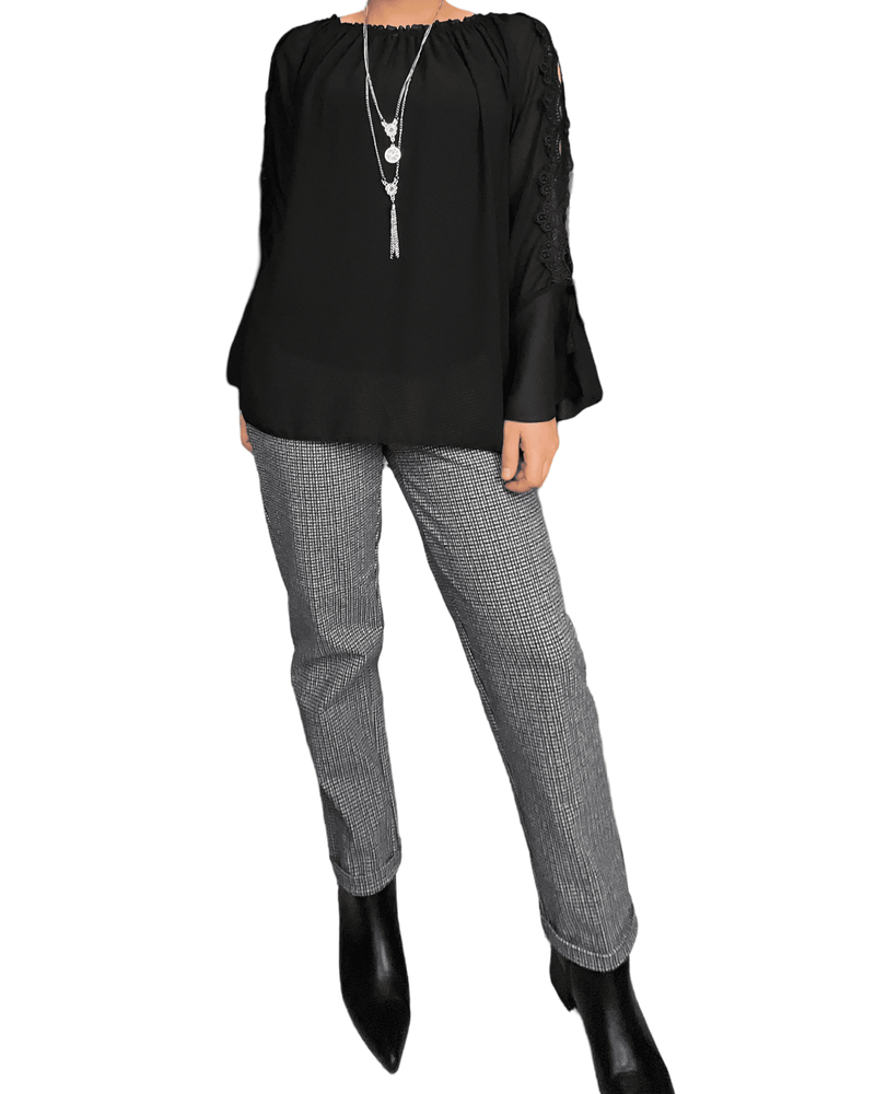 Pantalon à carreaux noirs, blancs et bruns pour femme avec blouse noire et collier long. 