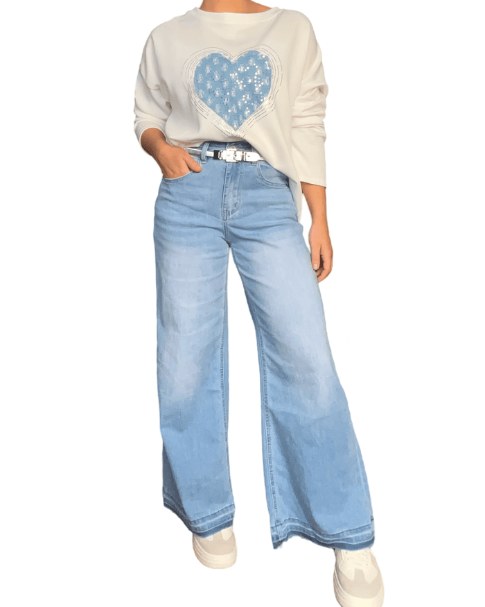 Chandail blanc cassé pour femme avec un cœur texturé bleu avec jeans ample et sneakers.